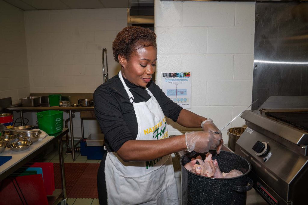 African woman preparing raw chicken in large pot