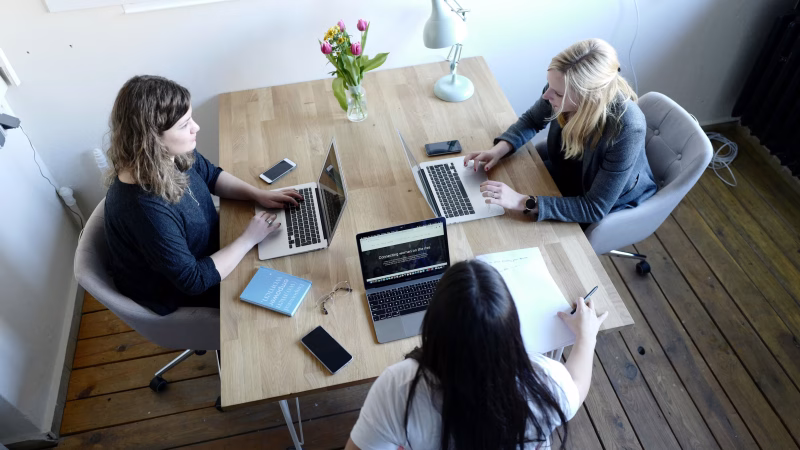 Group of women sitting at a table working on laptops