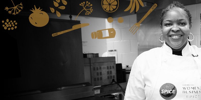 Front profile of a smiling woman wearing an apron and chef jacket standing in an industrial kitchen